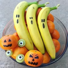 oranges and bananas with faces painted on them are in a glass bowl next to other fruit