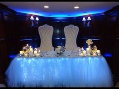 two white chairs sitting on top of a blue table covered in tulle and candles