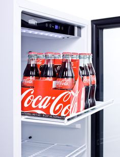 an open refrigerator with six cans of coca - cola in it