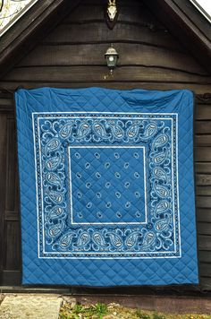 a blue and white quilt hanging on the side of a wooden building in front of a house