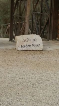 a sign that reads jordan river in arabic on the ground next to a wooden structure