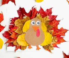 a turkey made out of leaves on top of a white surface with fall leaves around it