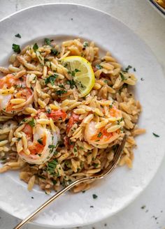 a white plate topped with pasta and shrimp next to a lemon wedge on top of a table