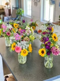 several vases filled with different colored flowers on a counter top in a kitchen or dining room