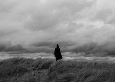 a person standing on top of a grass covered hill under a cloudy sky with clouds