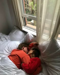 two children sleeping on a bed in front of a window