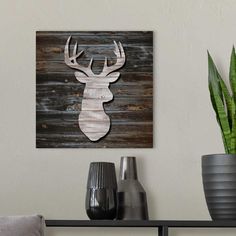 a wooden deer head mounted on a wall next to two vases and a potted plant