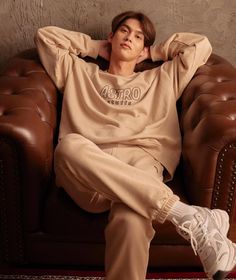 a young man sitting on top of a brown leather chair wearing a sweatshirt and sweatpants