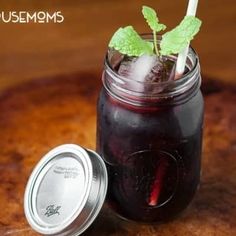 a mason jar filled with red liquid and mint sprigs on top of a wooden table