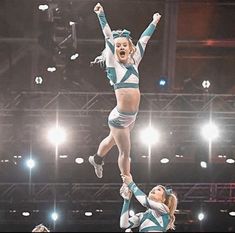 two cheerleaders are performing in the air with their hands up and feet apart