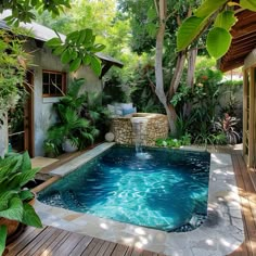 an outdoor swimming pool surrounded by greenery and wooden decking, with a waterfall in the middle