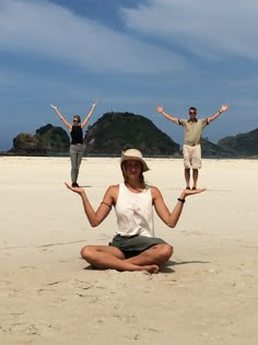 three people sitting on the beach with their arms in the air and one person standing behind them