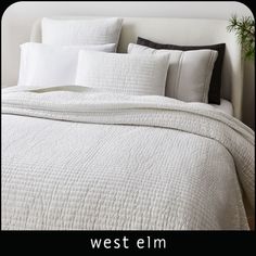 a bed with white linens and pillows on top of it, next to a potted plant