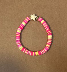 a pink and yellow beaded bracelet with a white flower on the end, sitting on a brown surface