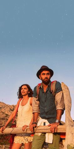 a man and woman standing next to each other on a wooden bench in the desert