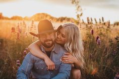 a man and woman hugging in the middle of a field with wildflowers at sunset