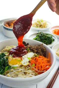 someone is dipping sauce on some noodles in a bowl with carrots and spinach