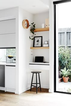 a kitchen with white walls and open shelves on the wall, along with a bar stool