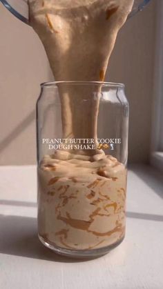 a person pouring peanut butter into a glass jar