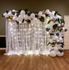 a balloon arch with white and gold balloons, greenery and lights on the wall