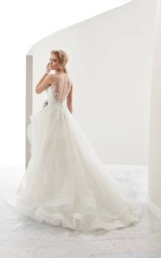 a woman in a white wedding dress is posing for the camera while leaning against a wall