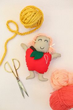 two balls of yarn are next to a doll and scissors on a white surface,