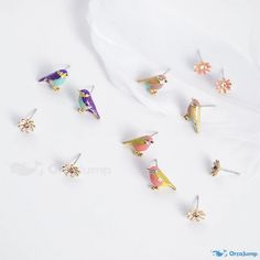 six pairs of colorful bird studs on a white surface with one earring in the middle