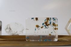 a glass block with flowers on it sitting on a wooden tray next to other vases