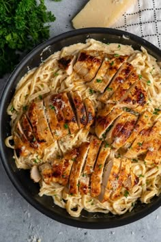 a pan filled with chicken and pasta next to parmesan cheese on a table