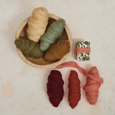 four different colored yarns in a wooden bowl on a white surface with one red, one green and one brown