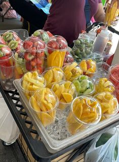 plastic cups filled with different types of fruit on top of a metal tray in front of people