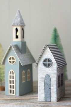 two small wooden houses sitting next to each other on top of a wood table with christmas trees in the background