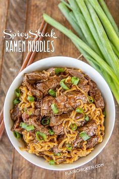 a bowl filled with noodles and beef on top of a wooden table next to green onions