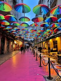 many colorful umbrellas are hanging from the ceiling in an open market area with tables and chairs