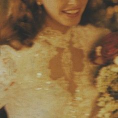 a woman in a white dress holding a bouquet of flowers and looking at the camera