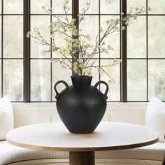 a black vase sitting on top of a wooden table next to a white couch and windows