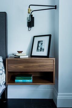 a wooden shelf with books on it next to a wall lamp and framed photograph in the corner