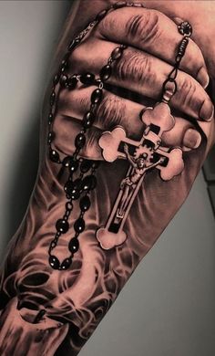 a man's hand holding a rosary and cross tattoo on his left upper arm