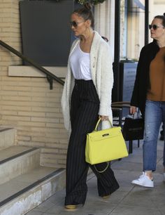 a woman carrying a yellow handbag while walking down the street with another woman behind her