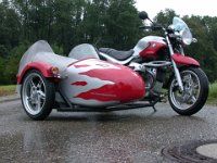 a red and silver motorcycle parked on top of a wet parking lot next to trees