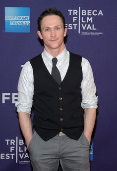 a man wearing a vest and tie standing in front of a purple wall at the tribe film festival