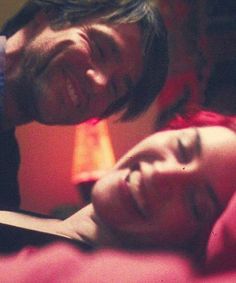 a man and woman laying in bed next to each other with their eyes closed, looking at the camera