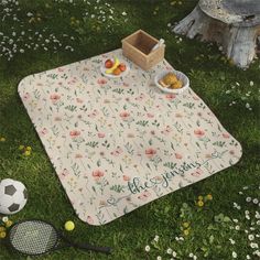 a picnic blanket on the grass with food and tennis racquets next to it