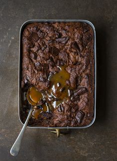 a brownie in a pan with caramel syrup on top and spoon next to it