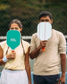 a man and woman holding paddles in front of their faces on a tennis court