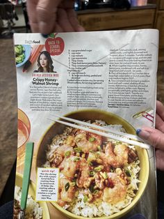 a person holding up a magazine with food on it and chopsticks in their hand