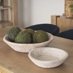 a bowl filled with moss sitting on top of a wooden table next to another bowl