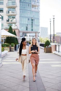 two women walking down the sidewalk in front of tall buildings