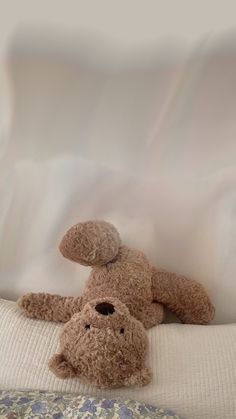 a teddy bear laying on top of a bed next to another stuffed animal in the corner