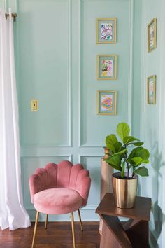 a pink chair sitting next to a green plant on top of a wooden table in front of a blue wall